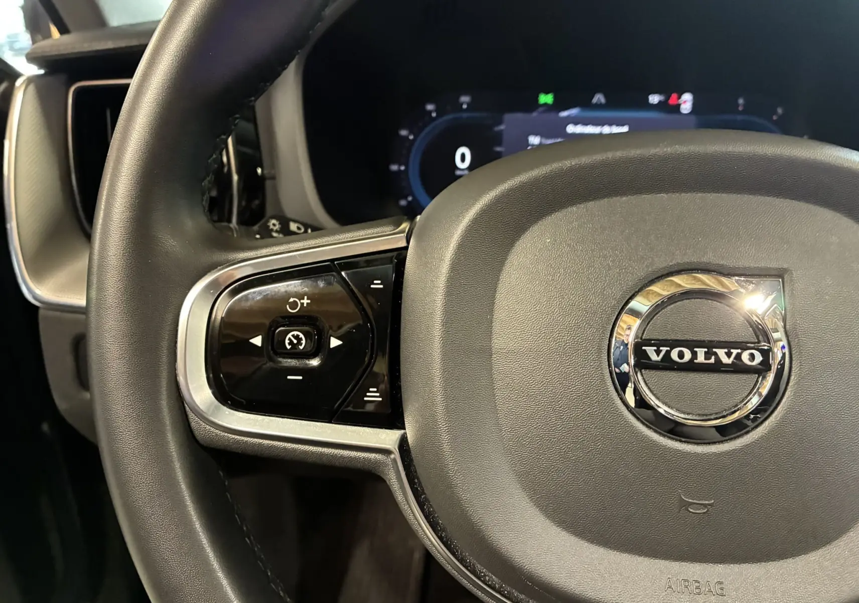 Gros plan sur le volant noir du Volvo XC60 2023 avec commandes intégrées et logo chromé au centre.