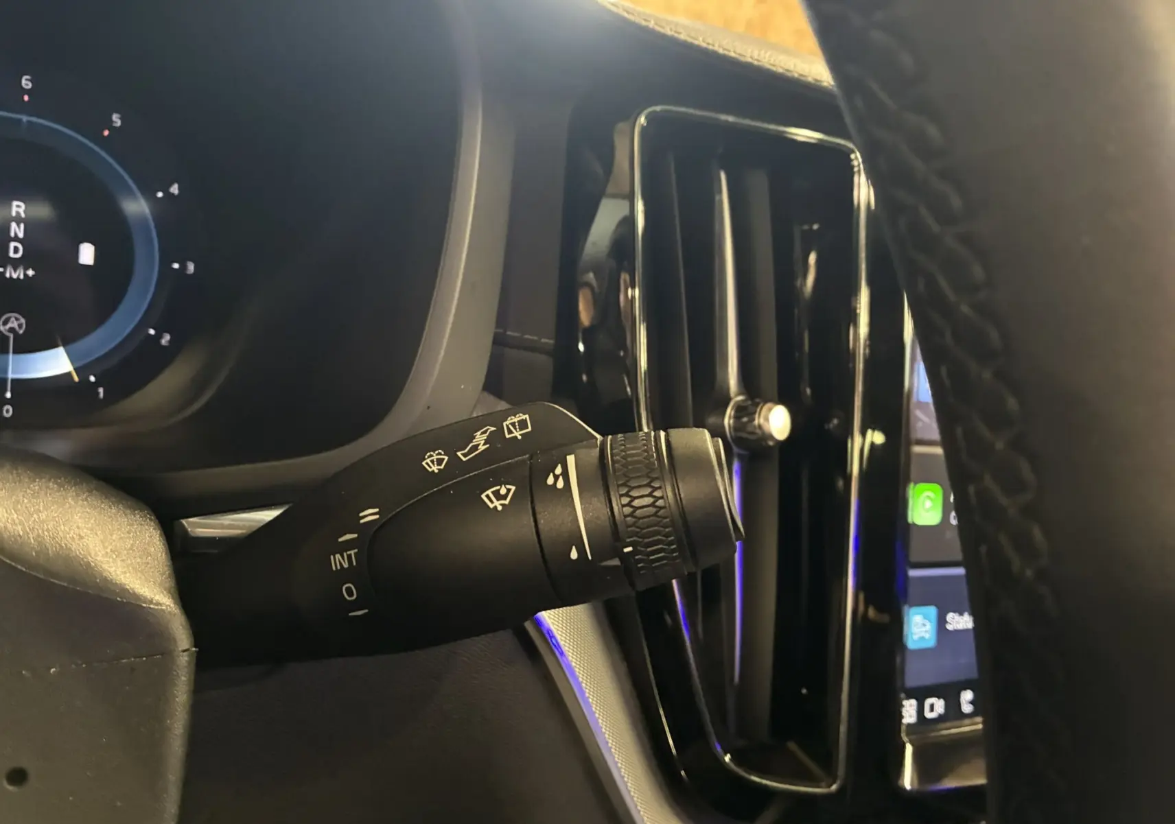 Gros plan sur la manette d’essuie-glace à gauche du volant dans l’habitacle noir du Volvo XC60 bleu 2023.
