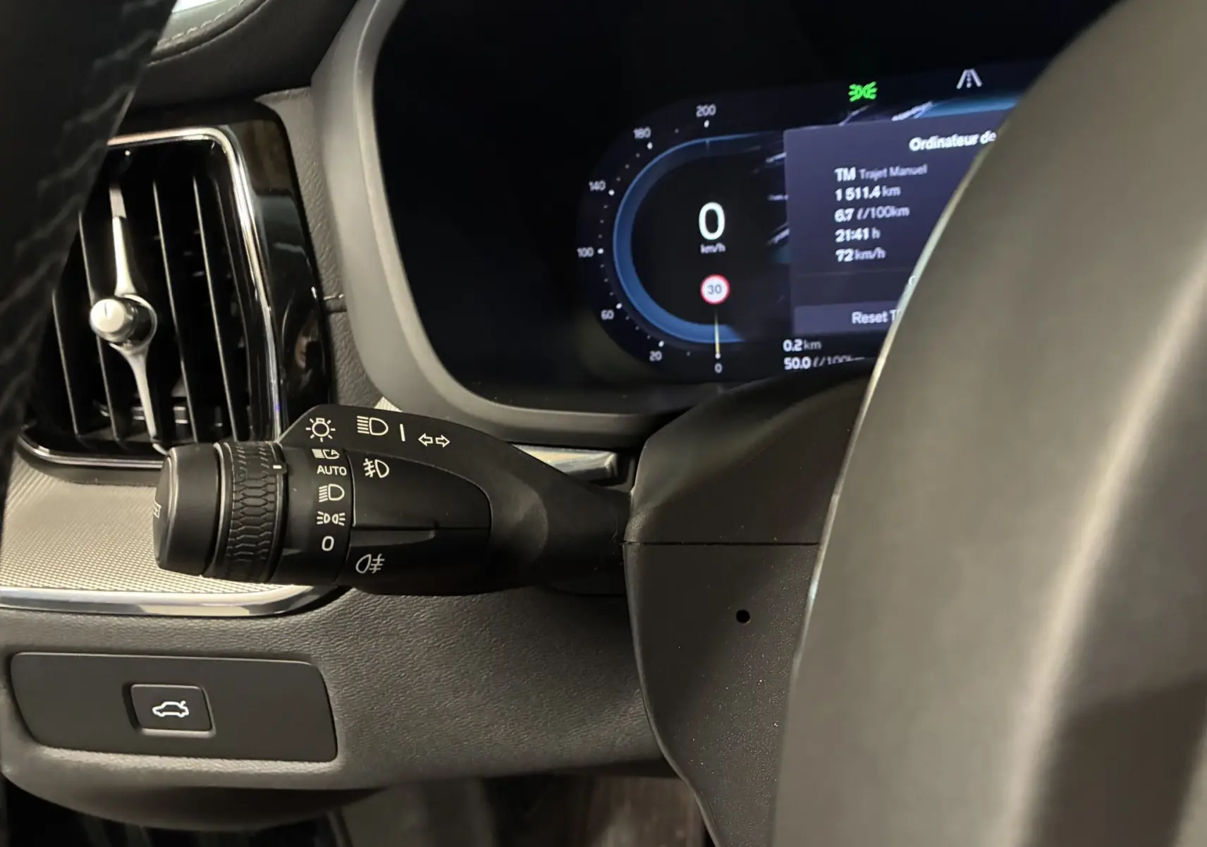 Gros plan sur la commande des phares et le tableau de bord numérique du Volvo XC60 2023, intérieur noir.