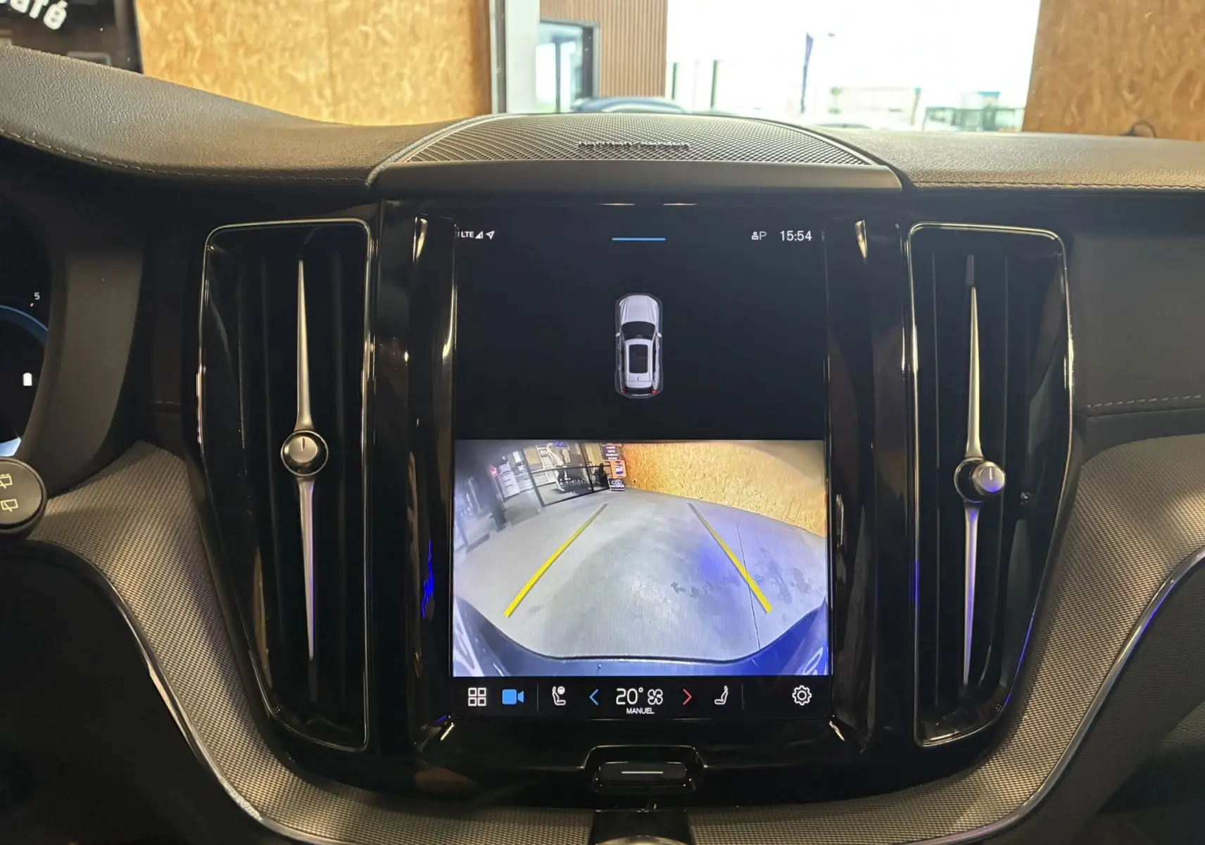 Vue intérieure centrée sur l'écran tactile affichant la caméra de recul du Volvo XC60 bleu, avec aérateurs noirs laqués.