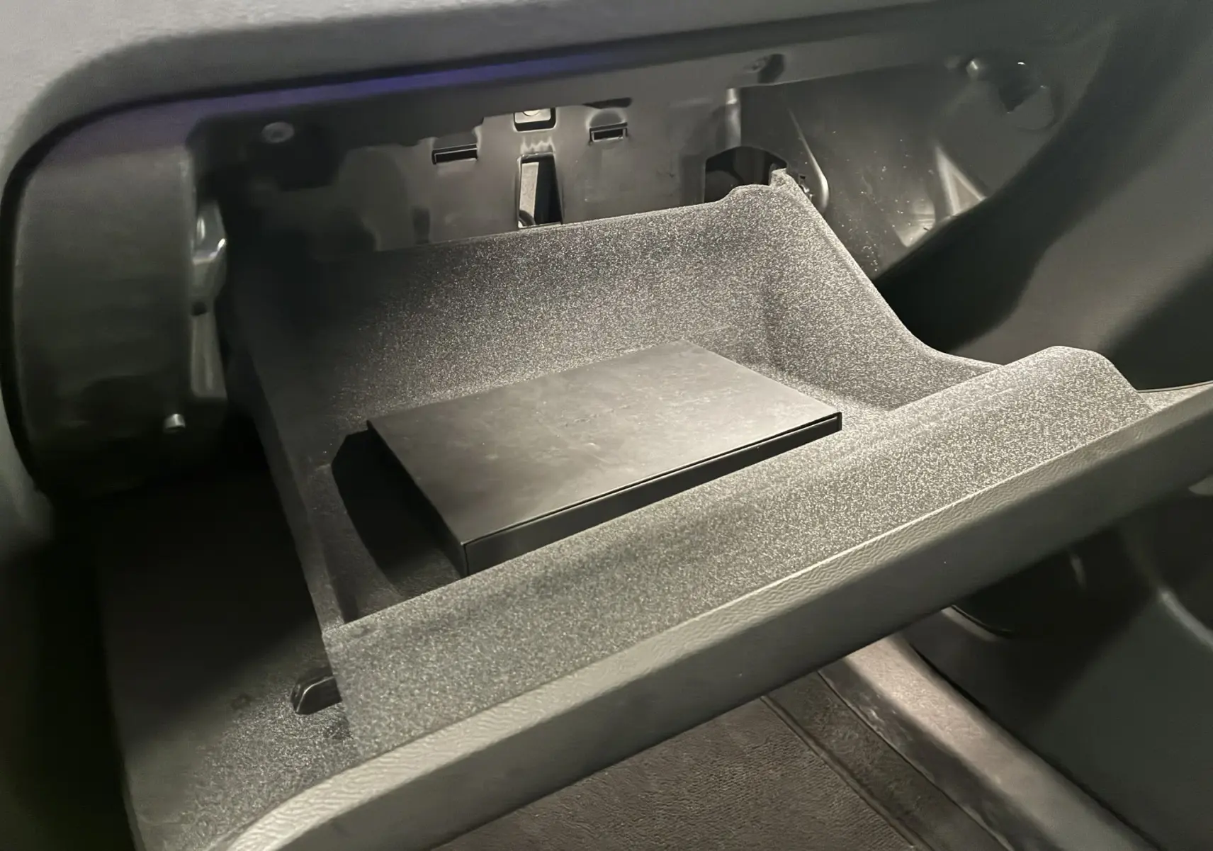 Gros plan sur la boîte à gants ouverte du Volvo XC60 2023, montrant un compartiment intérieur noir avec un objet rectangulaire.