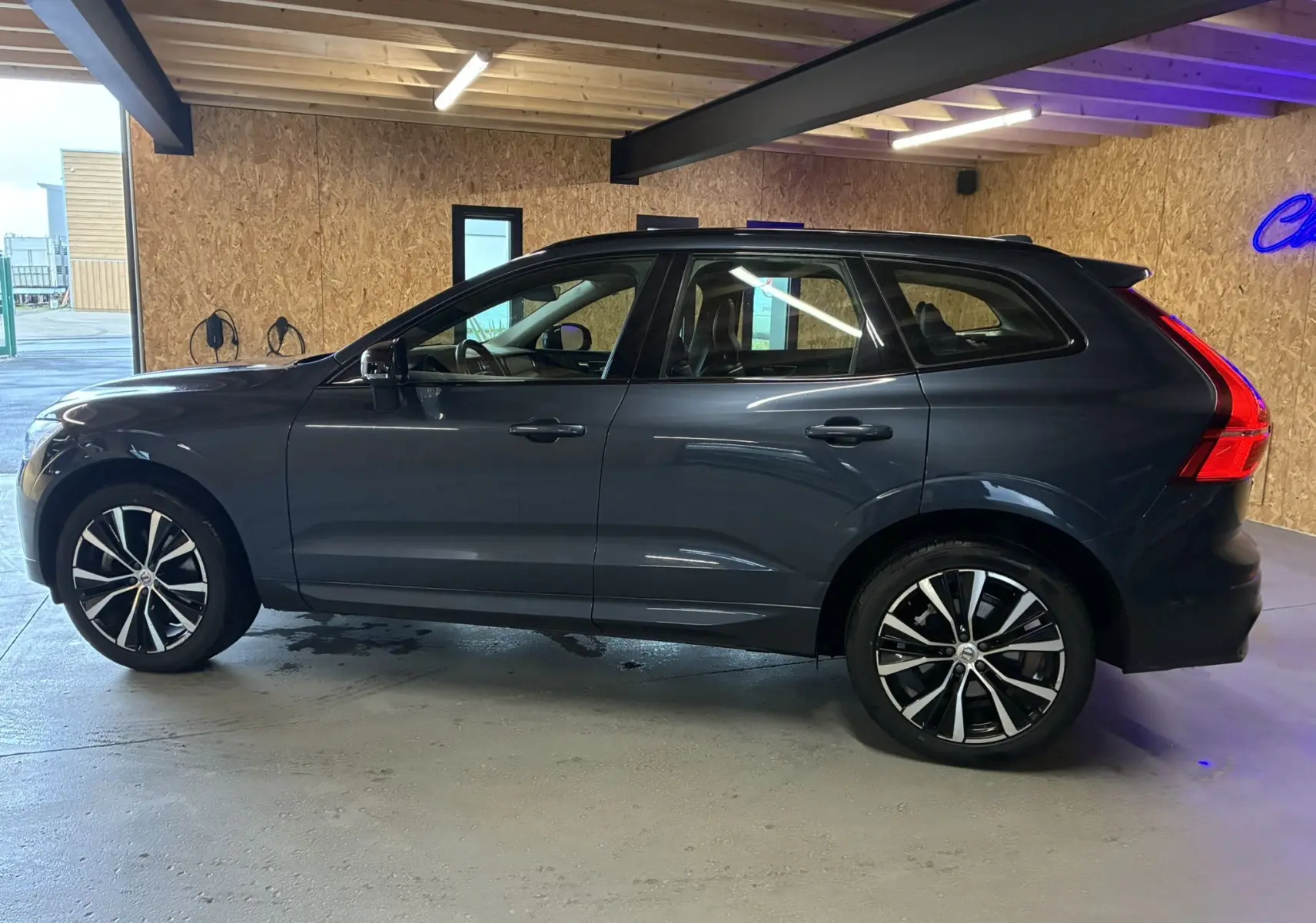 Vue latérale droite d'un Volvo XC60 bleu 2023 avec jantes alliage 20'' noir et diamant dans un garage.