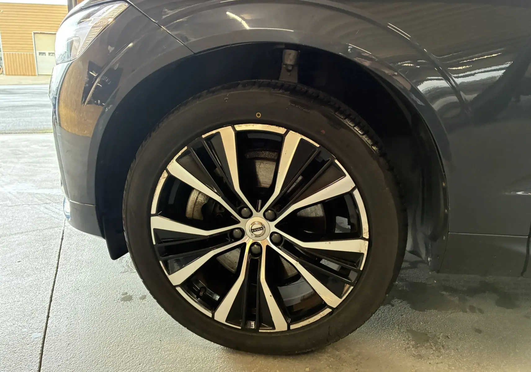 Gros plan sur la roue avant gauche du Volvo XC60 bleu 2023 avec jante alliage 20'' noir et diamant.