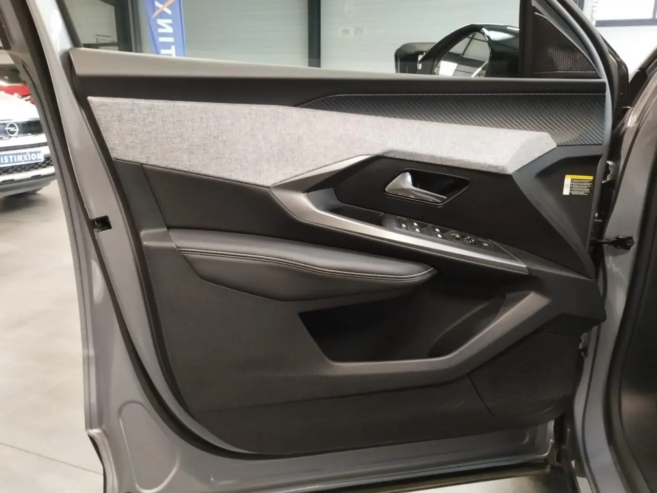 Vue intérieure de la porte avant gauche gris Artense du Peugeot 3008 2024 avec habillage tissu et commandes électriques.