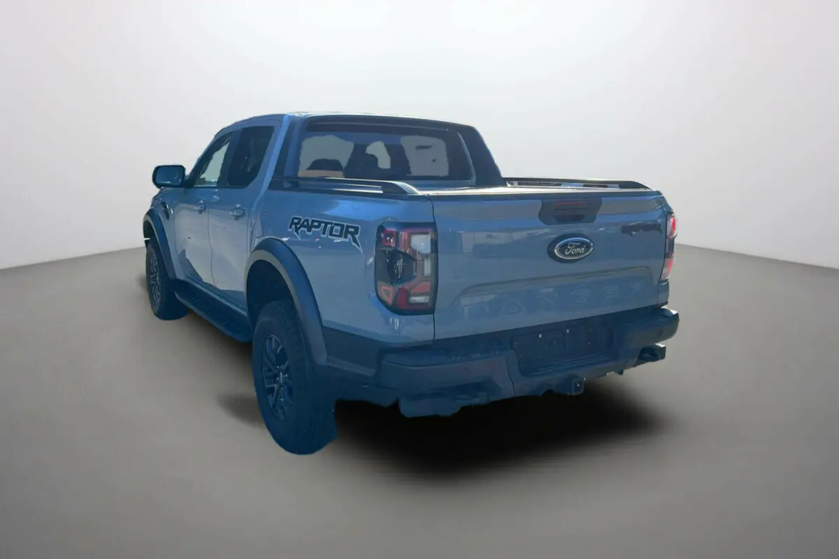 Vue 3/4 arrière du Ford Ranger Raptor gris commandeur avec logo Raptor sur la benne et jantes alu noires.