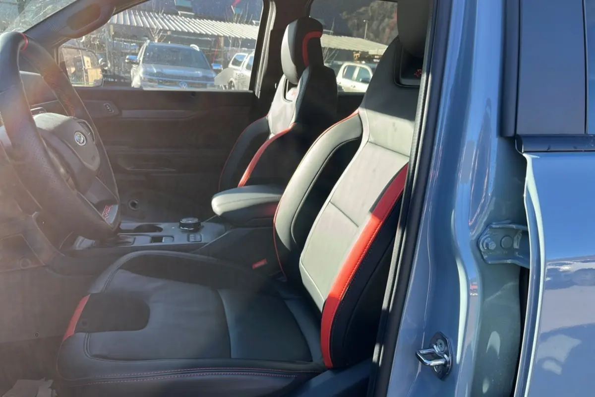 Vue intérieure côté conducteur du Ford Ranger Raptor gris commandeur, sièges sport cuir noir et rouge avec accoudoir central.
