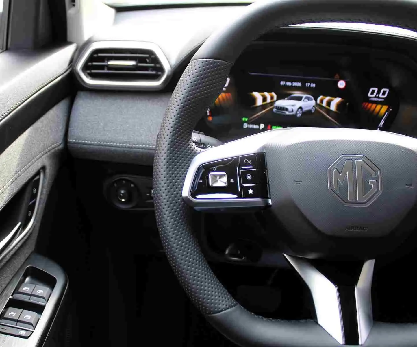 Vue intérieure centrée sur le volant perforé noir du MG ZS 1.5L Hybrid+ avec tableau de bord numérique affichant un véhicule blanc.