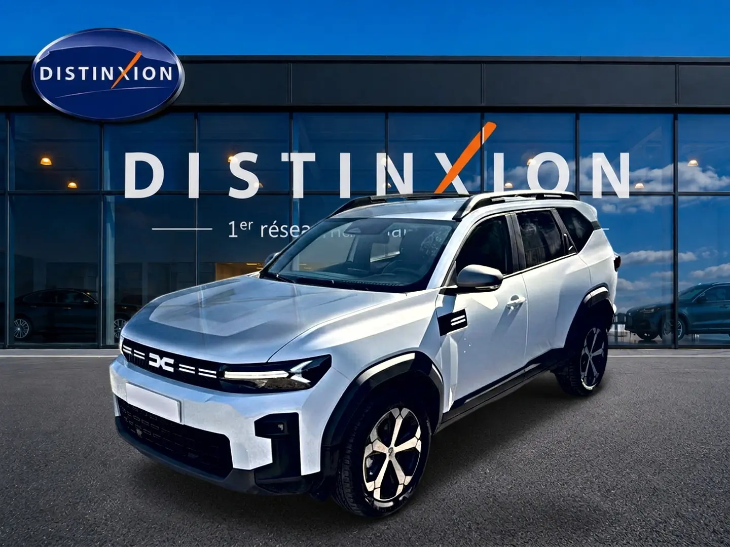 SUV Dacia Bigster blanc en 3/4 avant droit, avec barres de toit et jantes alu noires et argentées.