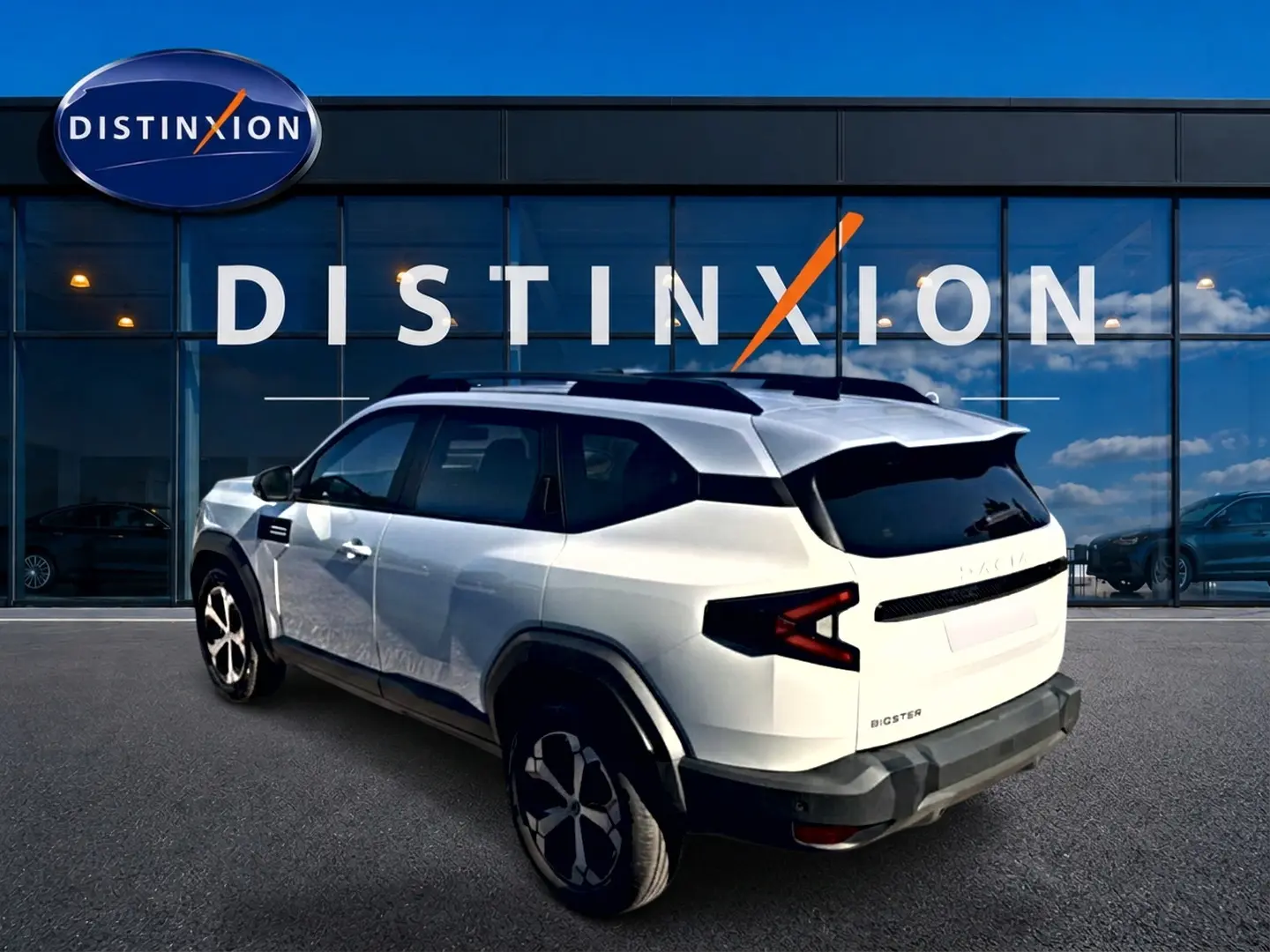Vue 3/4 arrière droite d'un Dacia Bigster blanc avec toit noir et jantes alu devant une vitrine Distinxion.