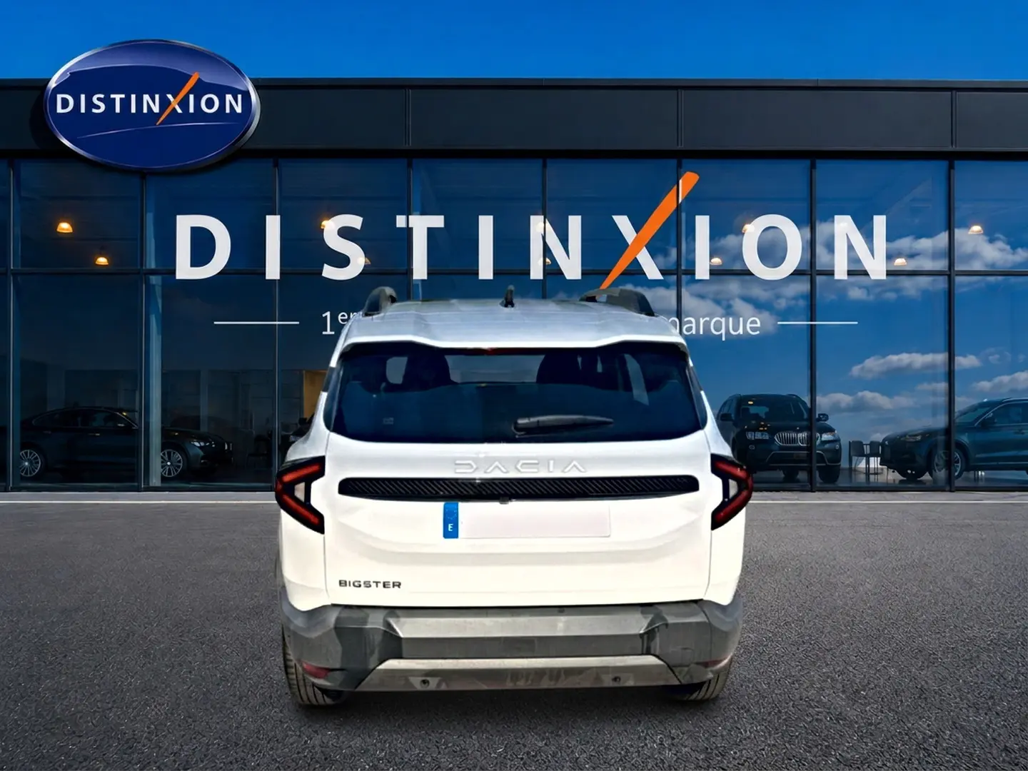 Vue arrière d'un Dacia Bigster blanc 2026 avec feux LED en forme de C et barres de toit visibles, devant une vitrine Distinxion.