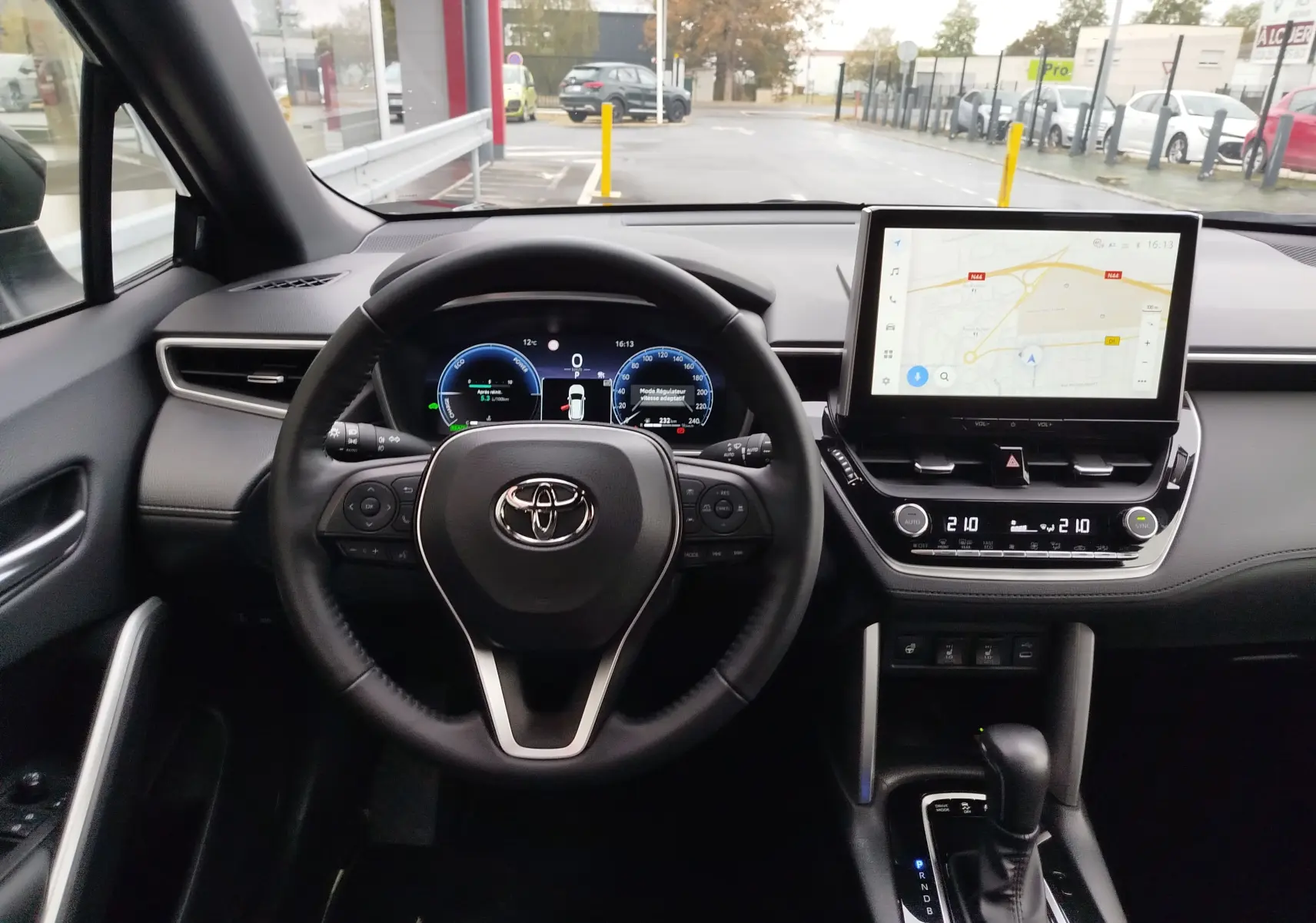 Vue intérieure centrée sur le volant et le tableau de bord numérique d’une Toyota Corolla Cross Hybrid 140 Luxury Limited noir.