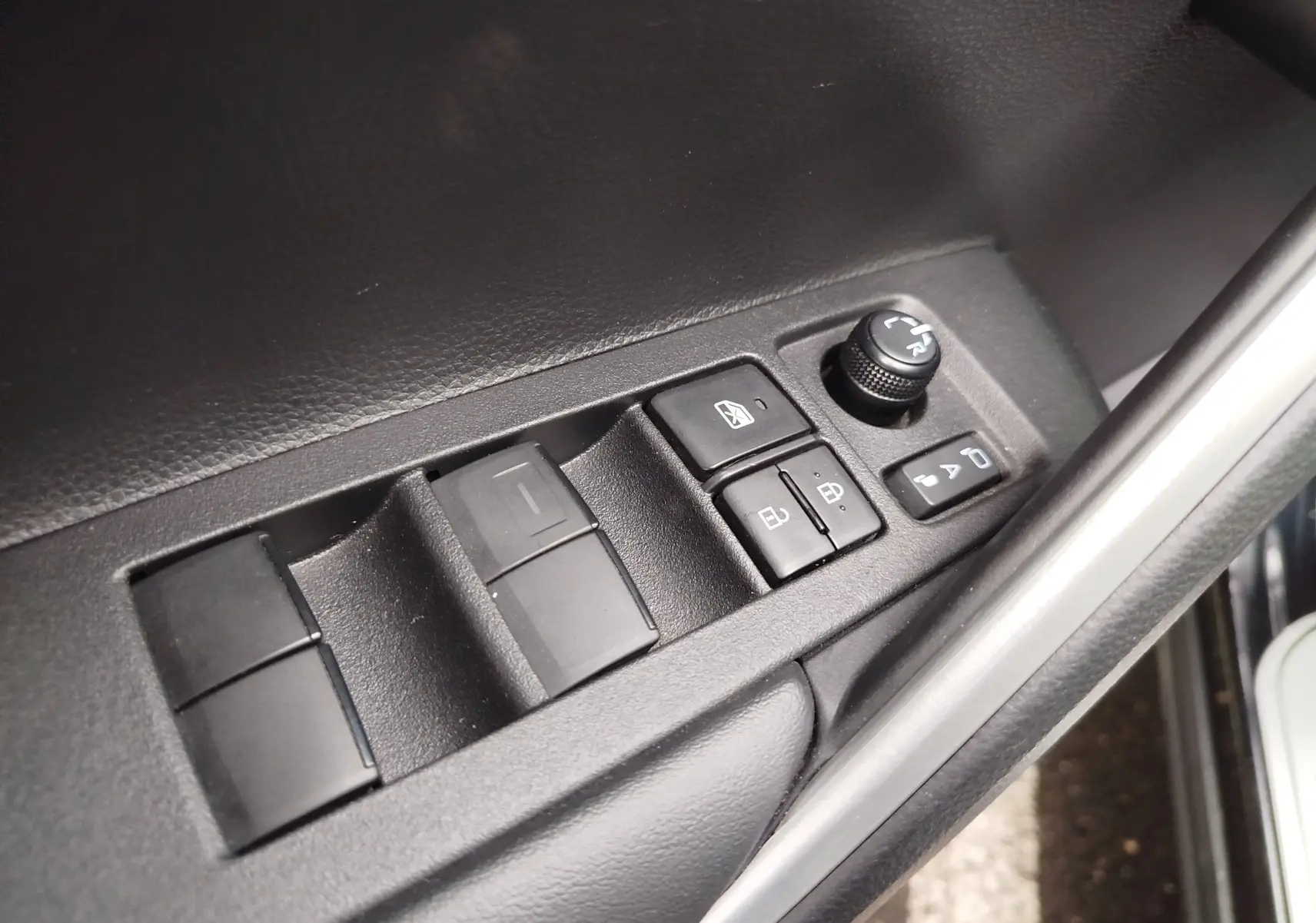 Gros plan sur les commandes des vitres et rétroviseurs côté conducteur d'une Toyota Corolla Cross Hybrid 140 Luxury Limited noire.