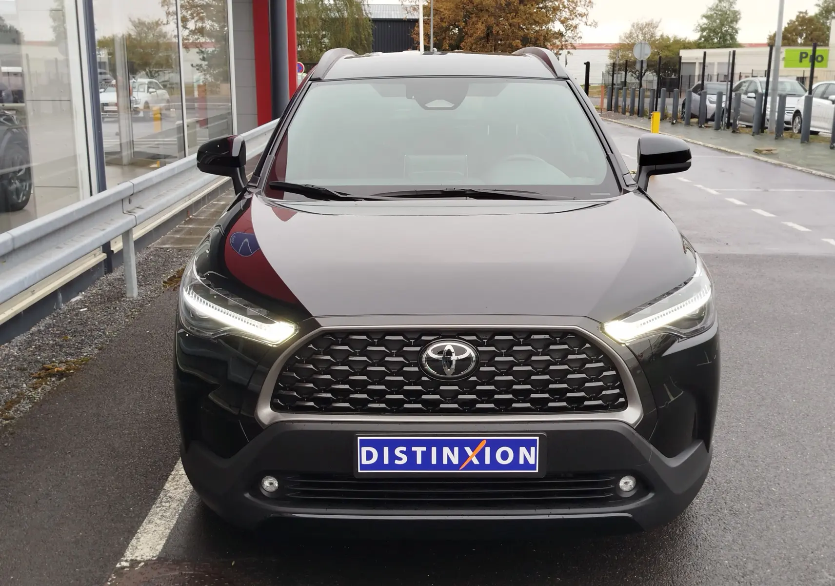 Vue avant d'une Toyota Corolla Cross Hybrid 140 Luxury Limited noire avec phares LED allumés sur un parking.