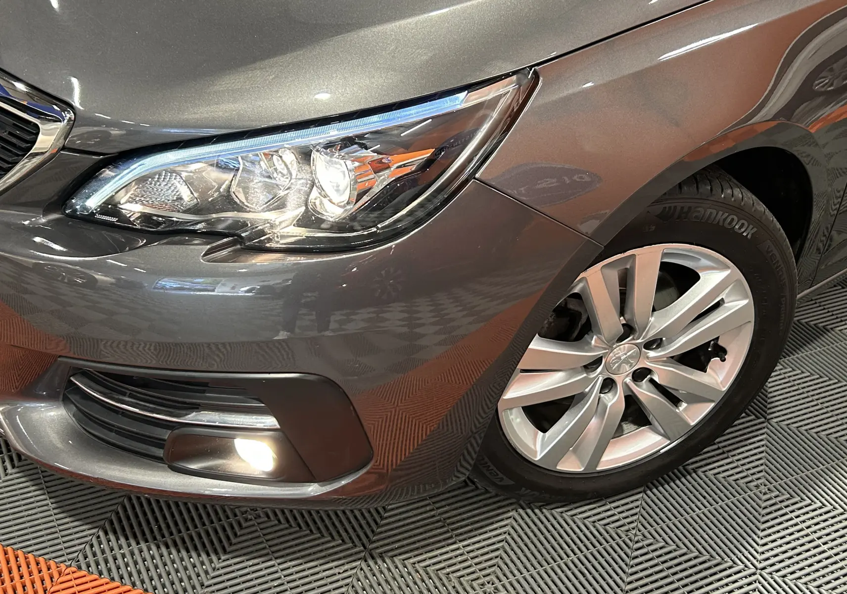 Gros plan sur l'avant droit gris métallisé d'une Peugeot 308 Active Pack 2021, avec phare et jante alliage visible.