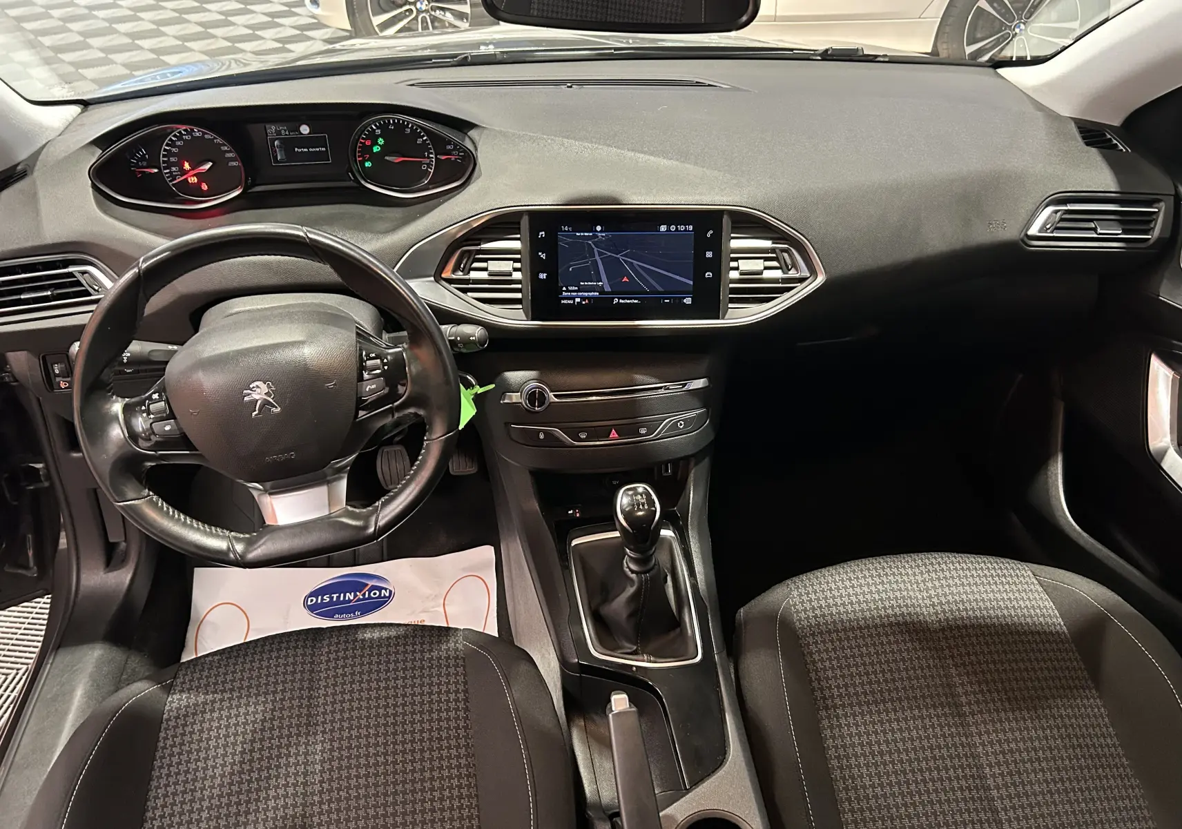 Vue intérieure avant de la Peugeot 308 Active Pack 2021, avec tableau de bord noir, volant multifonction et écran tactile central.
