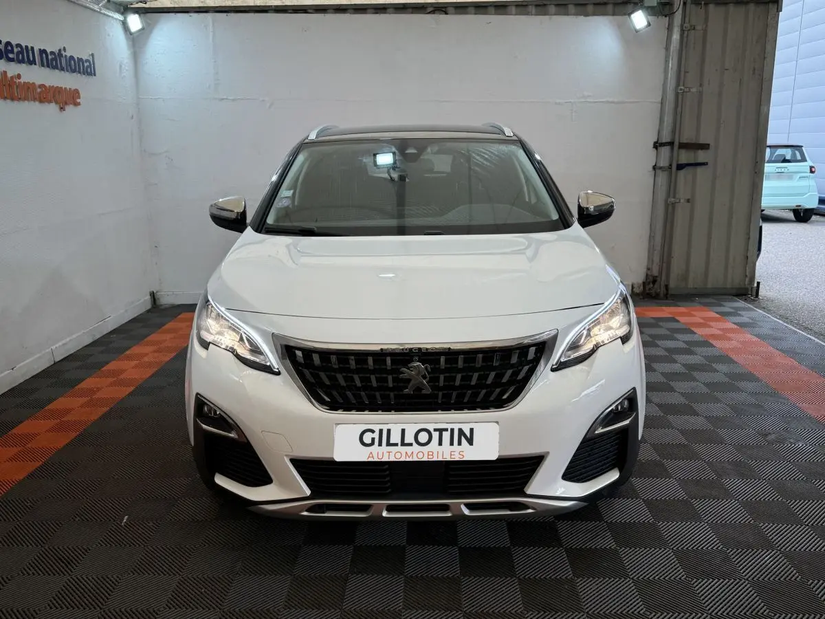 Peugeot 3008 blanc vue de face dans un garage avec calandre noire et phares allumés.