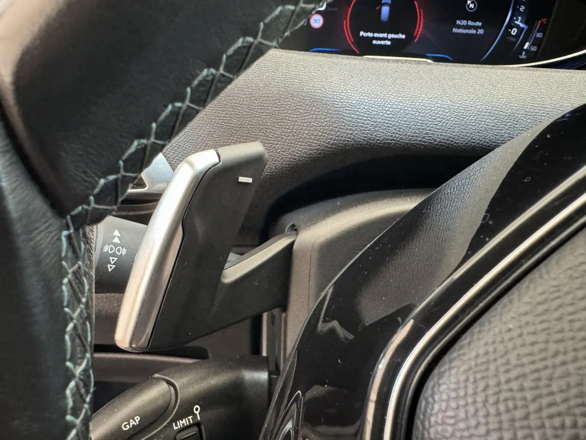 Gros plan sur le volant cuir et palettes de changement de vitesse du Peugeot 3008 blanc, tableau de bord numérique visible.