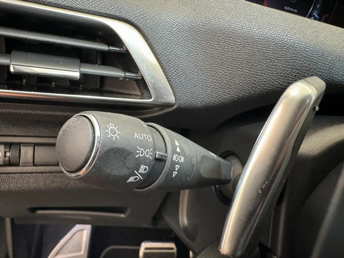 Gros plan sur la commande d'éclairage noire à gauche du volant dans l'habitacle d'un Peugeot 3008 blanc.