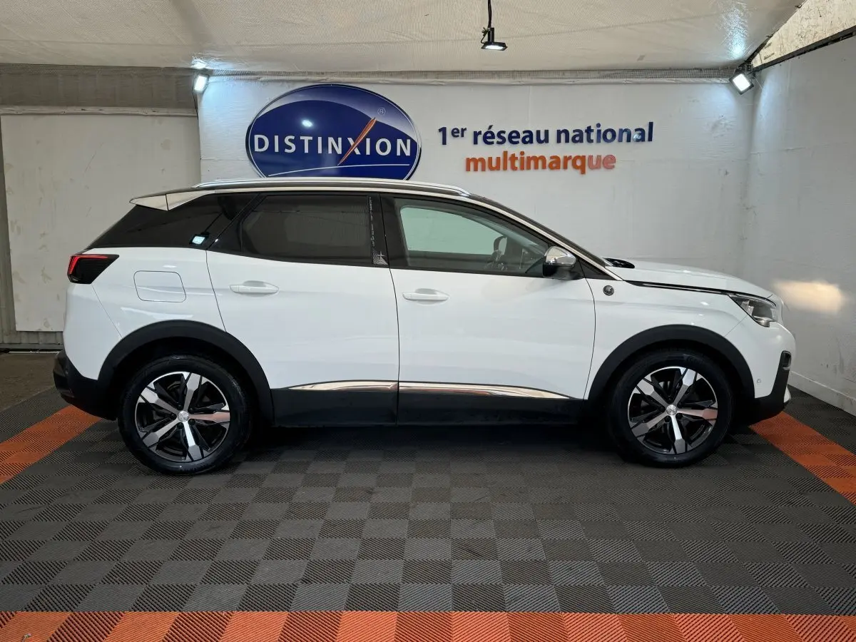 Vue latérale droite d'un Peugeot 3008 blanc avec jantes noires et toit noir dans un showroom.