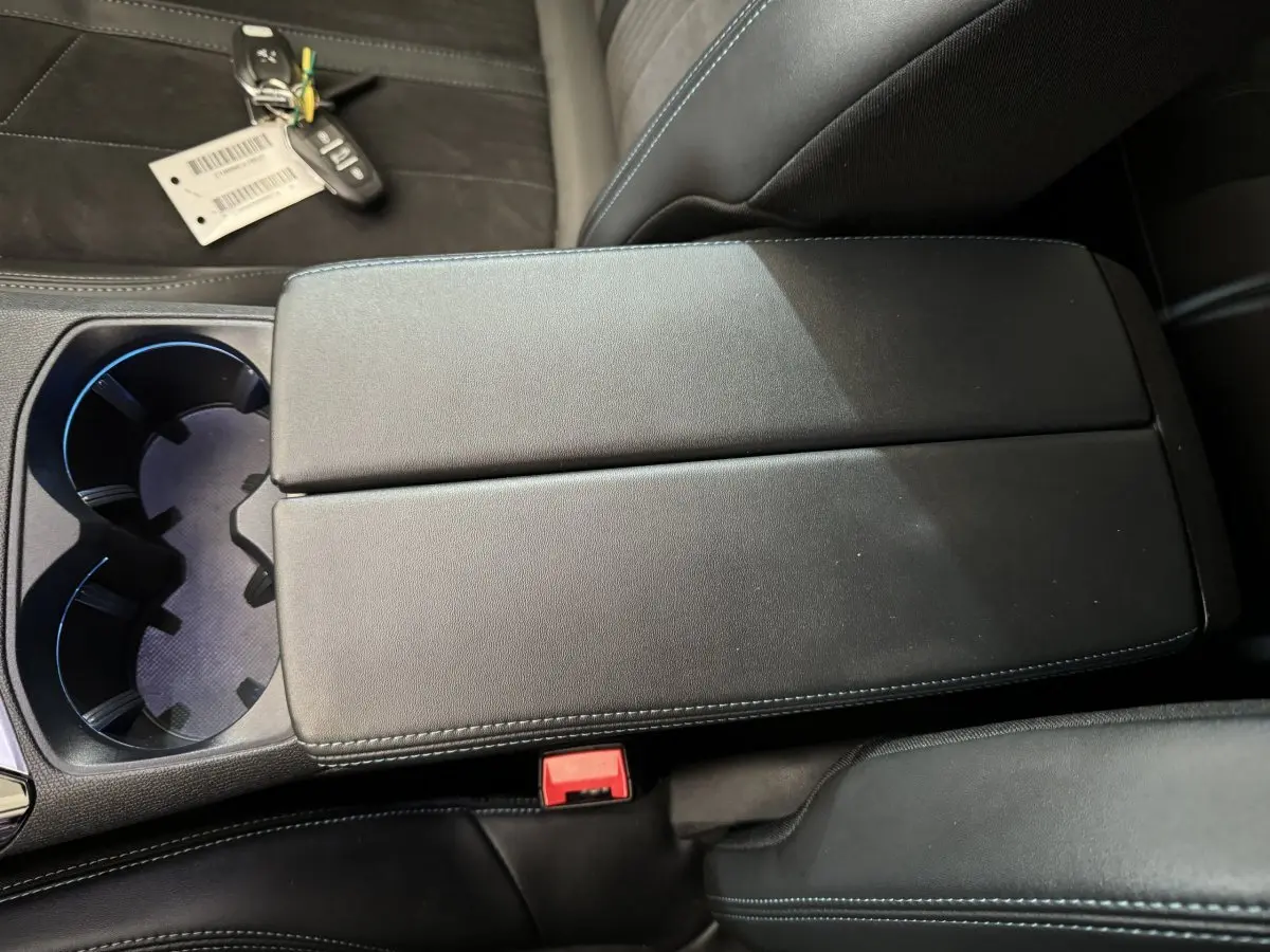 Gros plan sur l'accoudoir central noir avec surpiqûres bleues et porte-gobelets du Peugeot 3008 blanc 2019.
