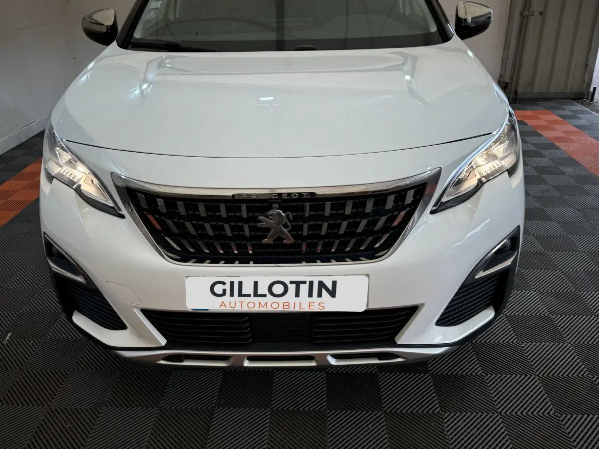 Vue avant rapprochée d’un Peugeot 3008 blanc avec calandre noire et phares LED allumés en intérieur.