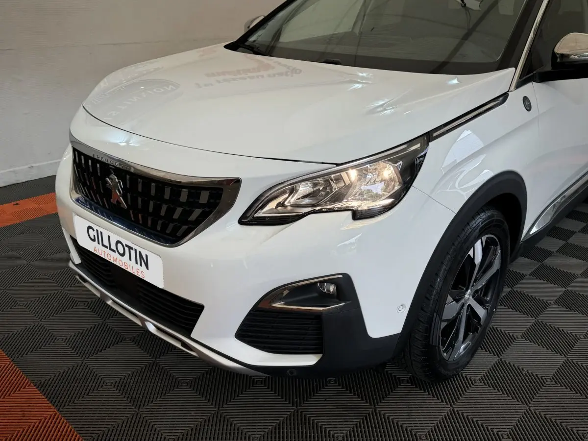 Vue 3/4 avant droit d'un Peugeot 3008 blanc avec calandre noire et phares allumés sur sol carrelé noir et orange.