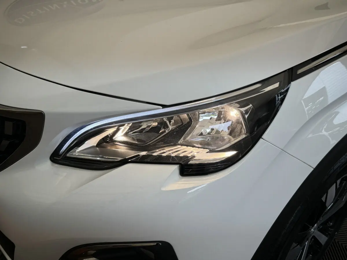 Gros plan sur le phare avant droit allumé du Peugeot 3008 blanc, soulignant les détails modernes du design.