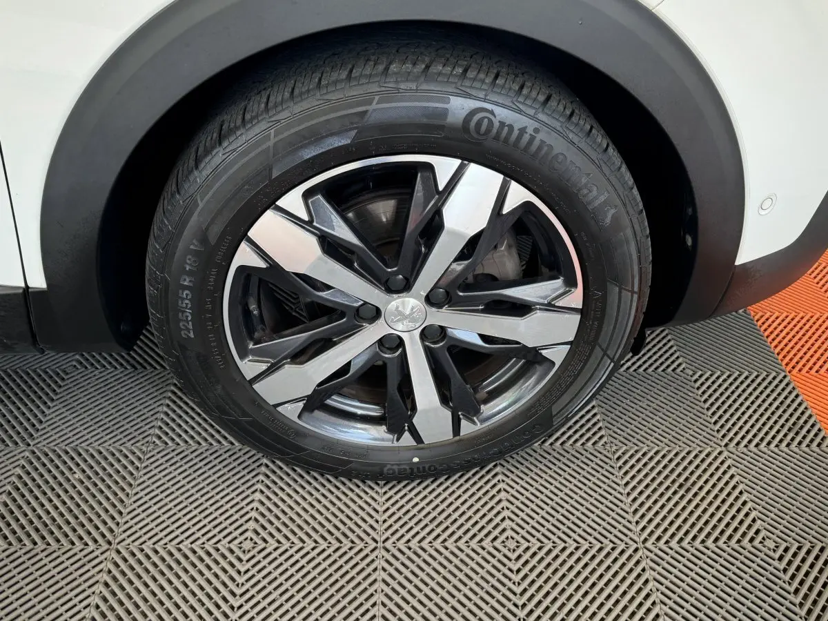 Gros plan sur la roue avant droite blanche d'un Peugeot 3008 avec jante alliage noire et argentée design moderne.