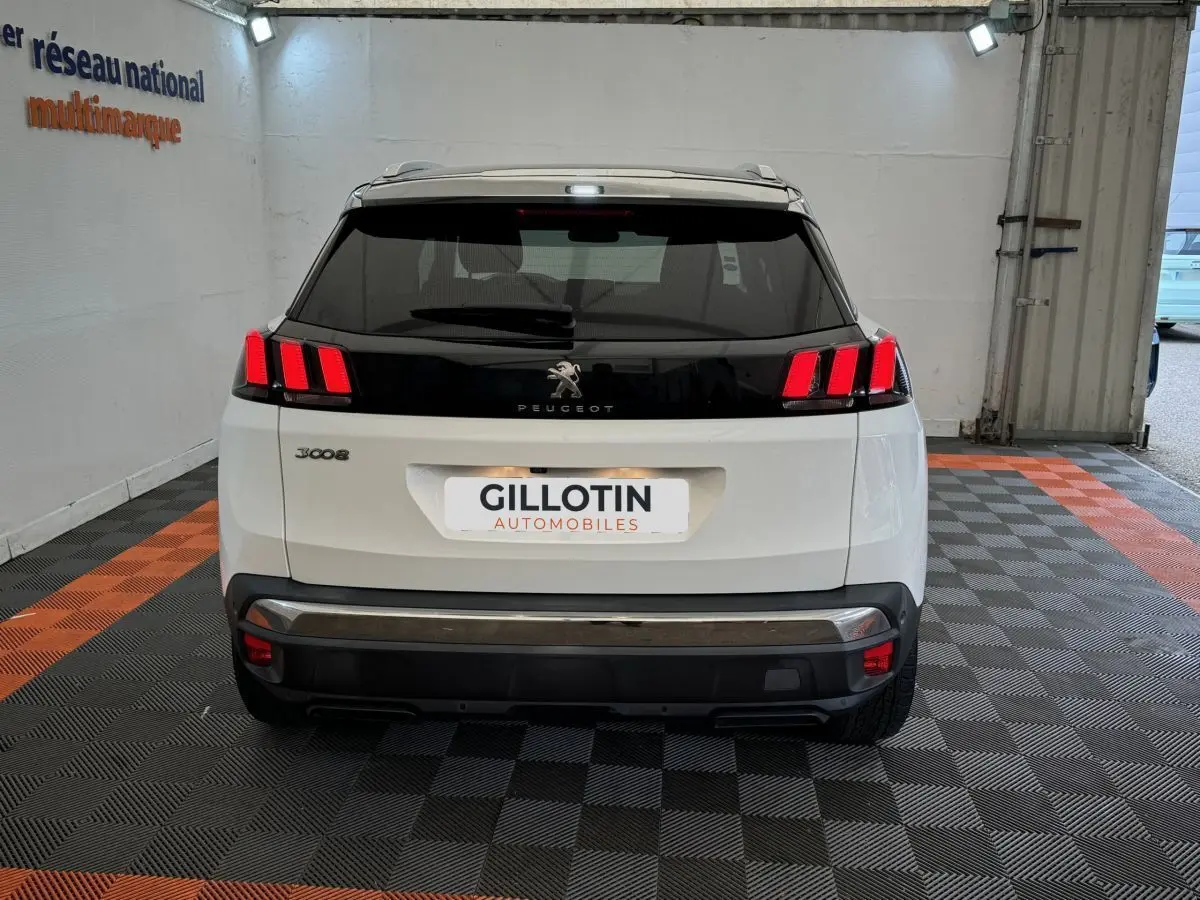 Vue arrière d'un Peugeot 3008 blanc avec feux arrière LED distinctifs et logo central sur bande noire.