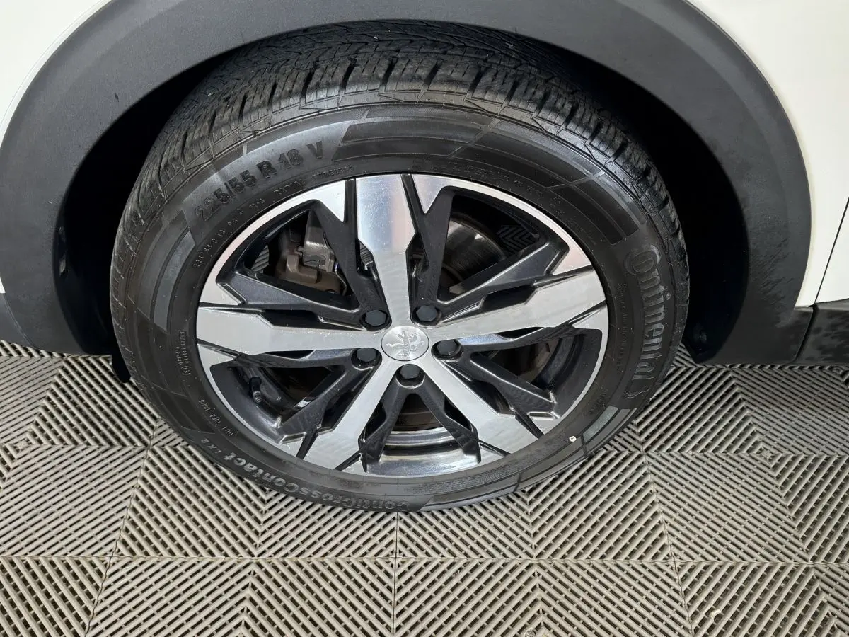 Gros plan sur la roue avant droite d'un Peugeot 3008 blanc, jante alliage bicolore et pneu Continental.
