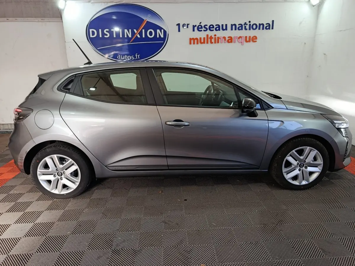 Profil droit d'une Renault Clio gris foncé 2025 Evolution Blue dCi 100, dans un showroom avec logo Distinxion en arrière-plan.