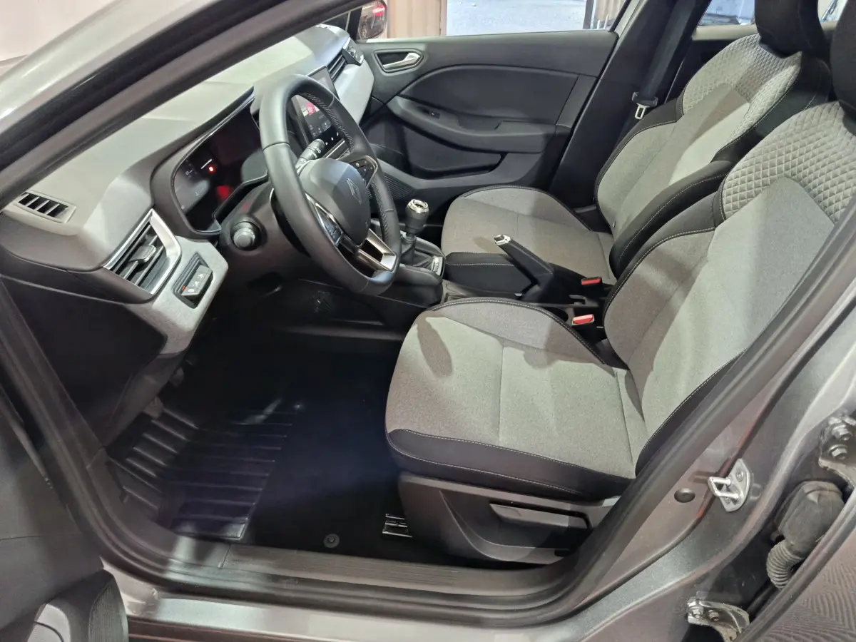 Intérieur côté conducteur de la Renault Clio gris foncé 2025, montrant sièges tissu bicolore et volant multifonctions cuir synthétique.