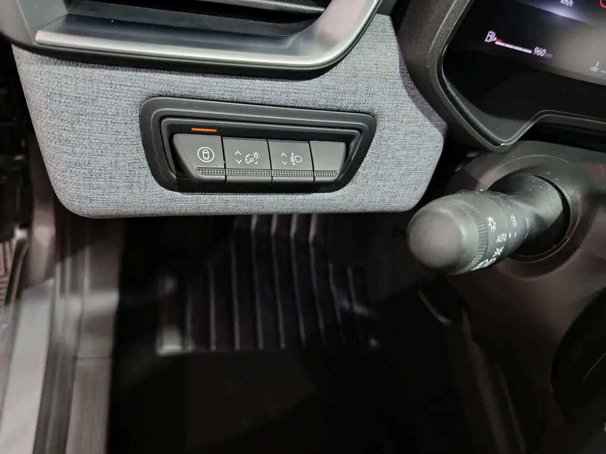 Gros plan sur les commandes d'éclairage et verrouillage sous le tableau de bord gris clair d'une Renault Clio 2025.