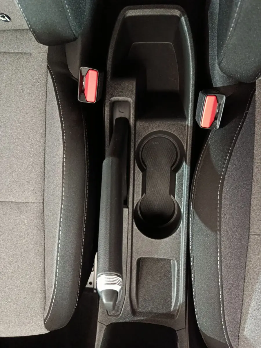 Vue plongeante sur la console centrale noire avec frein à main et ceintures rouges entre les sièges gris foncé Renault Clio 2025.