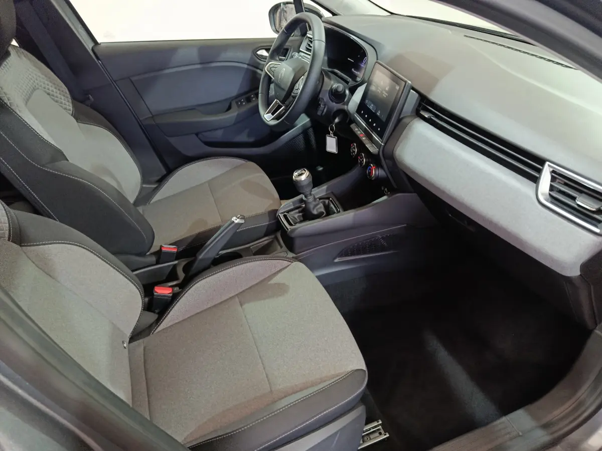 Intérieur avant droit de la Renault Clio gris foncé 2025, montrant sièges tissu, volant multifonctions et écran tactile central.