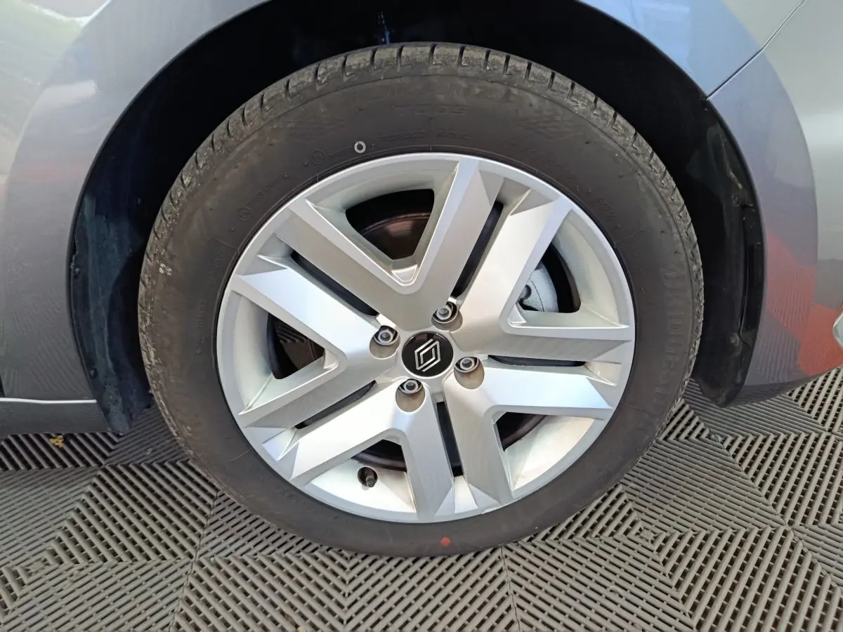 Gros plan sur la roue avant droite d'une Renault Clio gris foncé, mettant en valeur la jante alliage au design moderne.