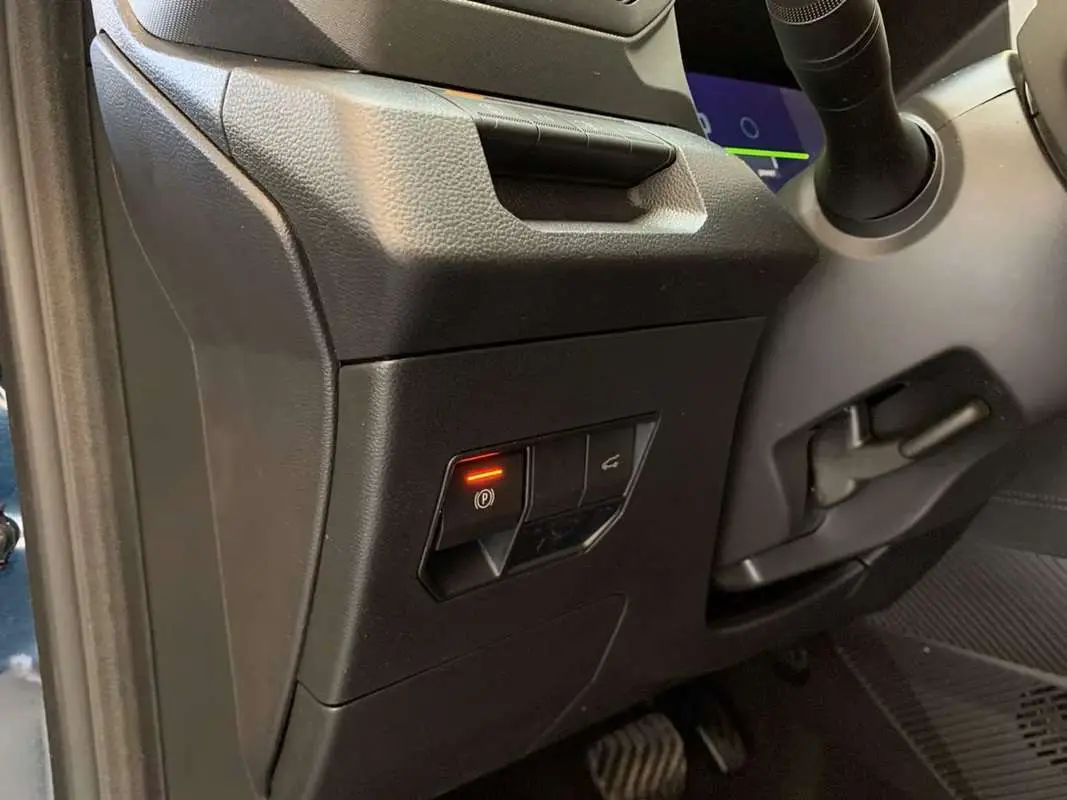 Détail intérieur du tableau de bord côté gauche du Dacia Bigster Hybrid 155 Journey Plus avec bouton frein à main électrique allumé.