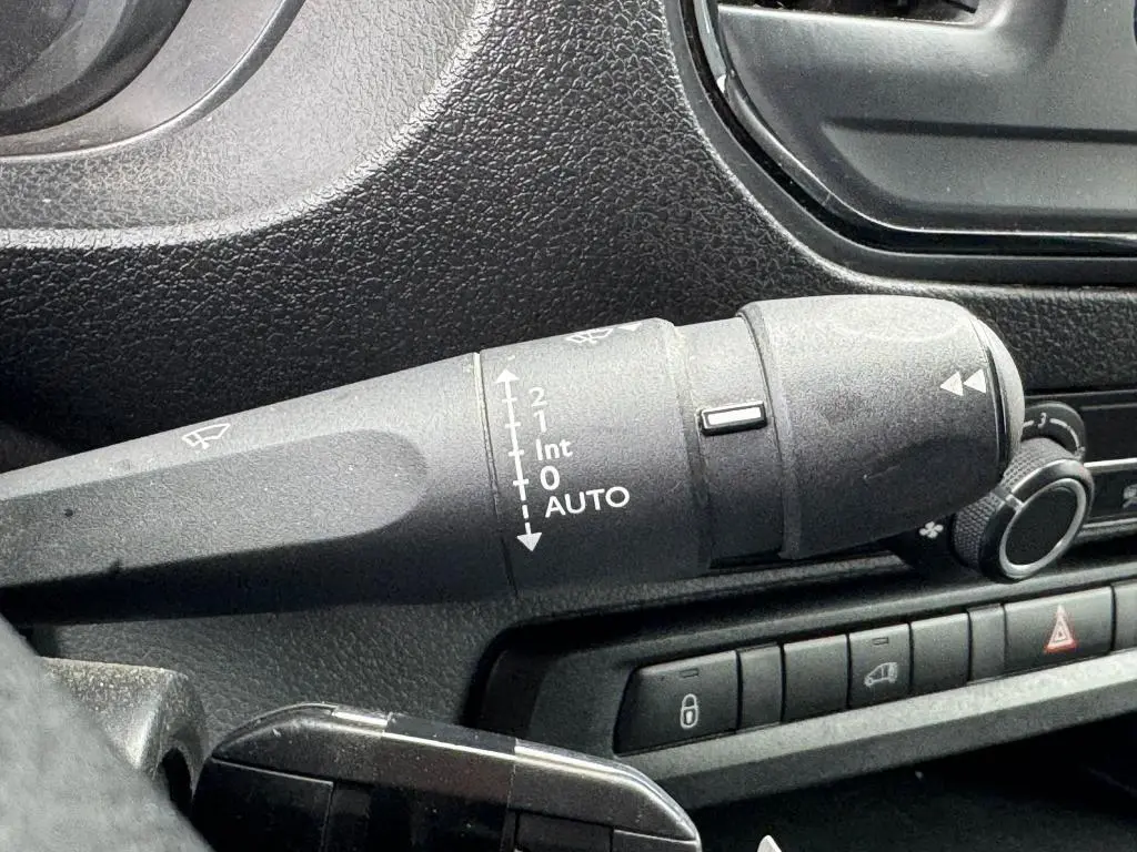 Gros plan sur la commande des essuie-glaces à gauche du volant dans l'habitacle noir du Peugeot Expert Fourgon blanc.