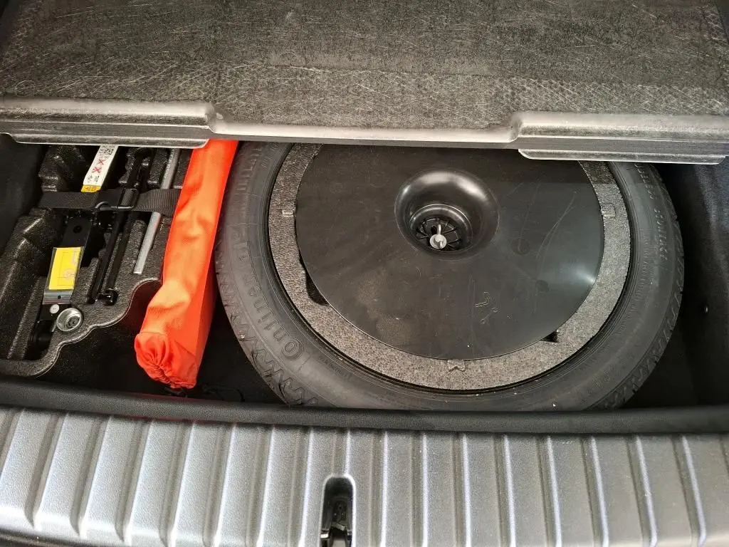 Coffre ouvert montrant la roue de secours et le kit de réparation dans une BMW Série 1 116d Business Design gris 2022.