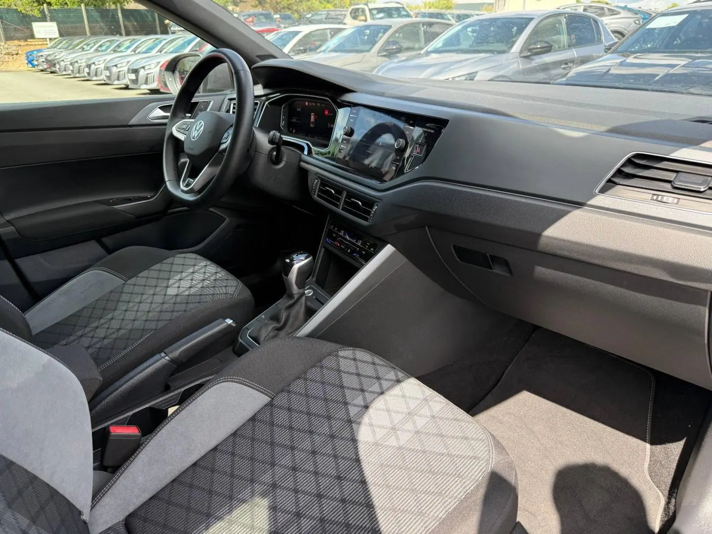 Vue intérieure côté conducteur du Volkswagen Taigo 2025, sièges tissu R-Line gris et tableau de bord moderne avec écran tactile.