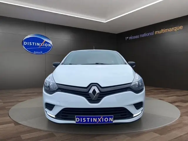 Vue frontale d'une Renault Clio IV blanche 2019 en showroom avec logo Distinxion visible sur le mur et la plaque.