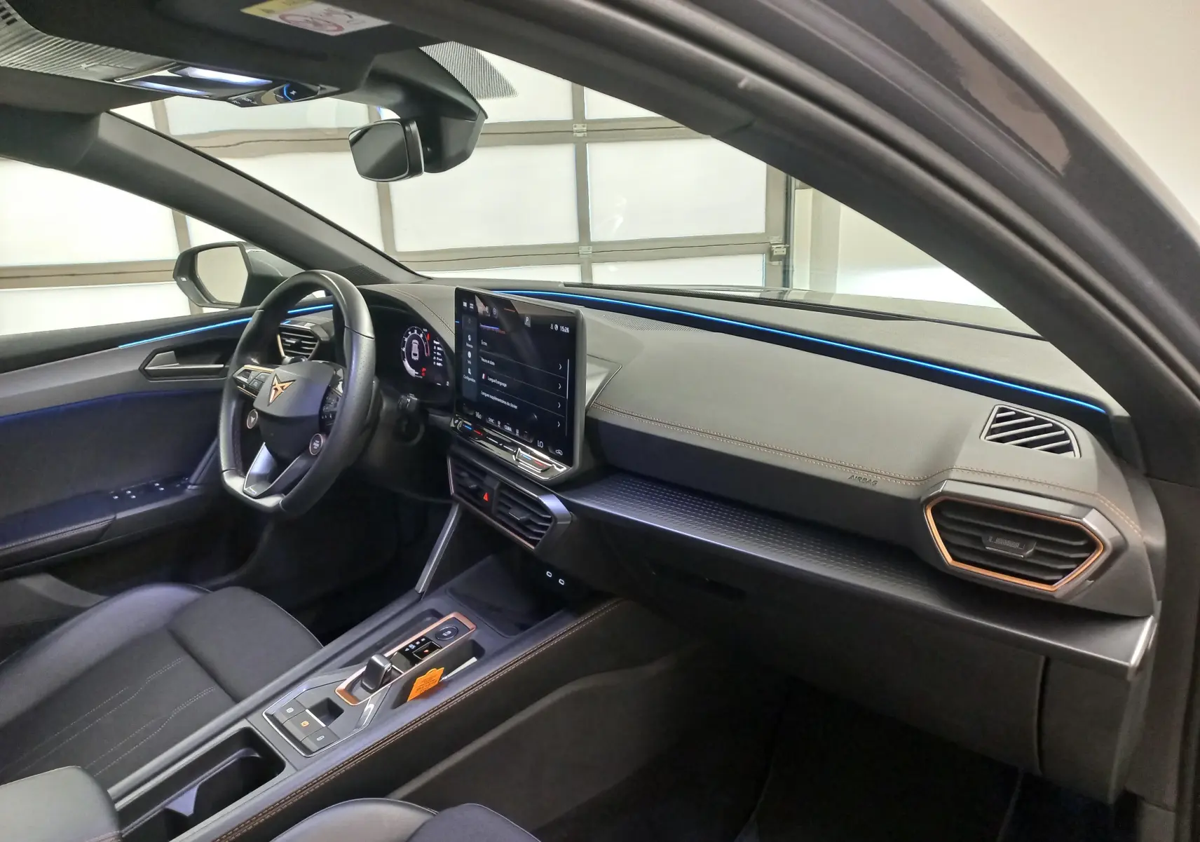 Vue intérieure côté conducteur de la CUPRA Leon Phase 2 avec éclairage d’ambiance bleu et finitions modernes.