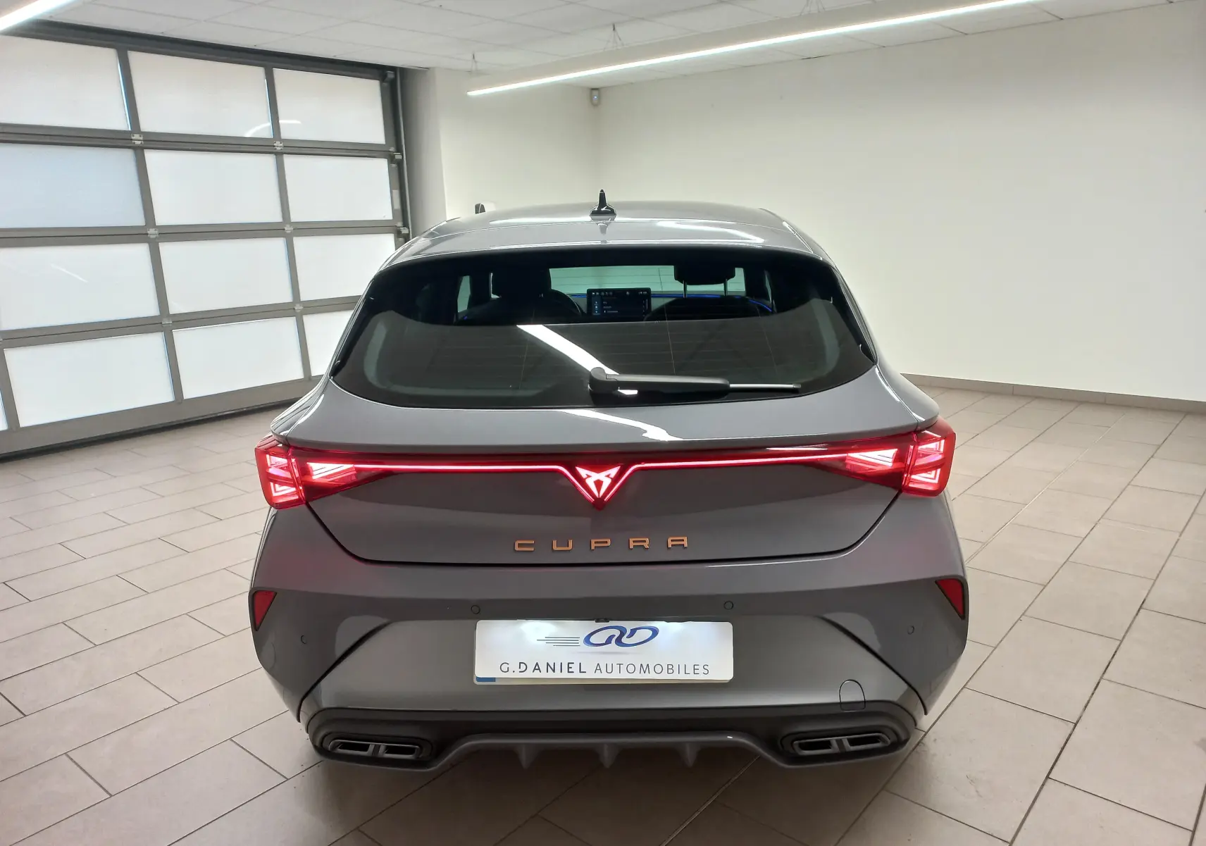 Vue arrière d'une CUPRA Leon Phase 2 gris Graphene avec feux arrière LED reliés et double sortie d'échappement intégrée.