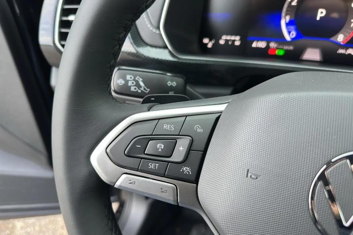 Gros plan sur le volant cuir multifonctions côté gauche du Volkswagen T-Cross noir intense avec commandes de régulateur adaptatif.