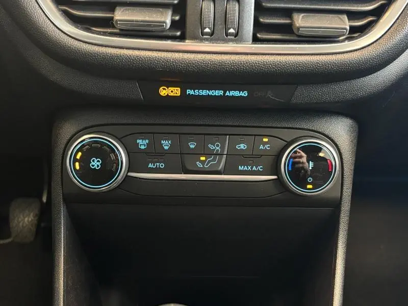 Vue rapprochée de la console centrale de la Ford Fiesta 2022 en Fashion Gris Magnetic, montrant les commandes de climatisation et l'indicateur airbag passager.