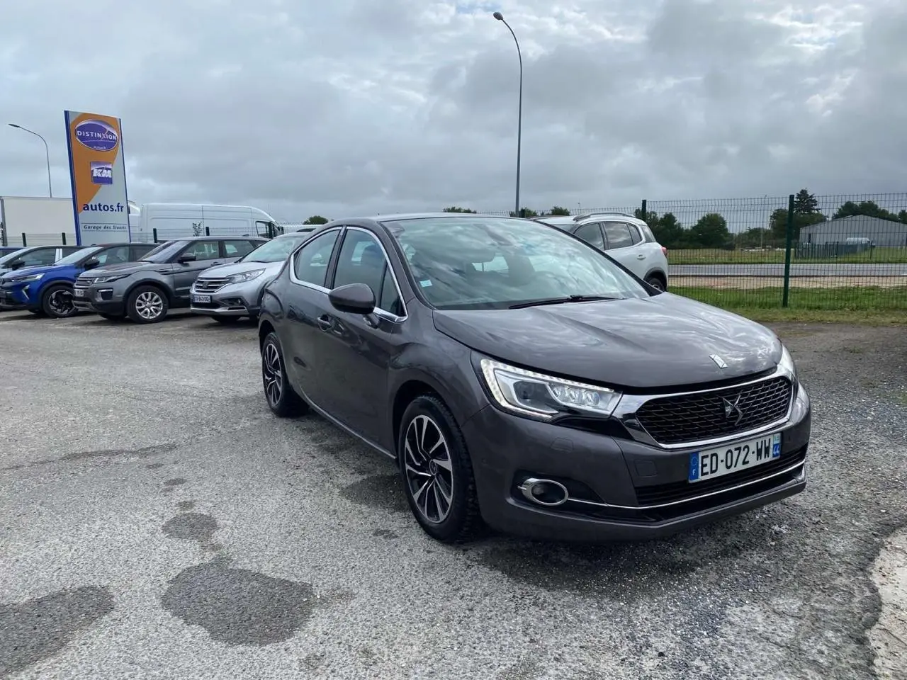 DS4 gris clair vue 3/4 avant droit sur parking avec calandre noire et jantes alliage distinctives.