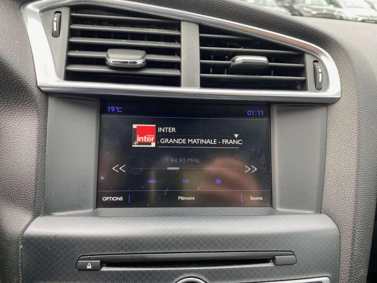 Écran tactile central affichant la radio dans l'habitacle du DS4 gris clair, vue rapprochée du tableau de bord.