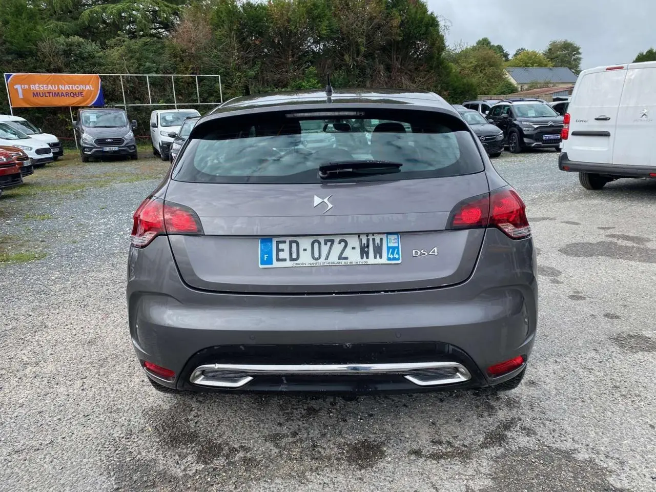 Vue arrière d'une DS4 gris clair avec feux rouges et double sortie d'échappement chromée sur un parking.