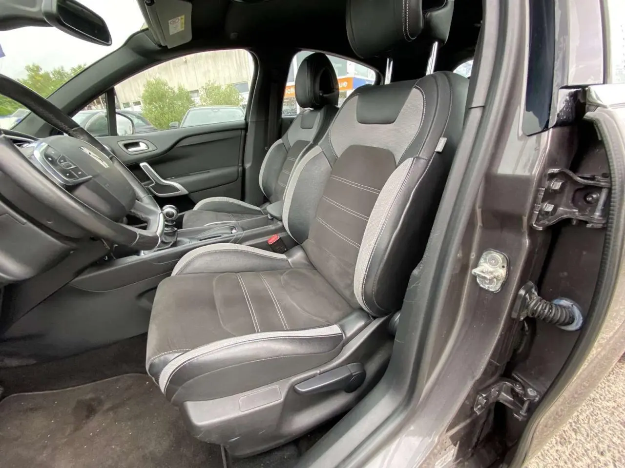 Vue intérieure côté conducteur du DS4 gris clair de 2016, montrant les sièges en tissu et alcantara noirs avec surpiqûres grises.