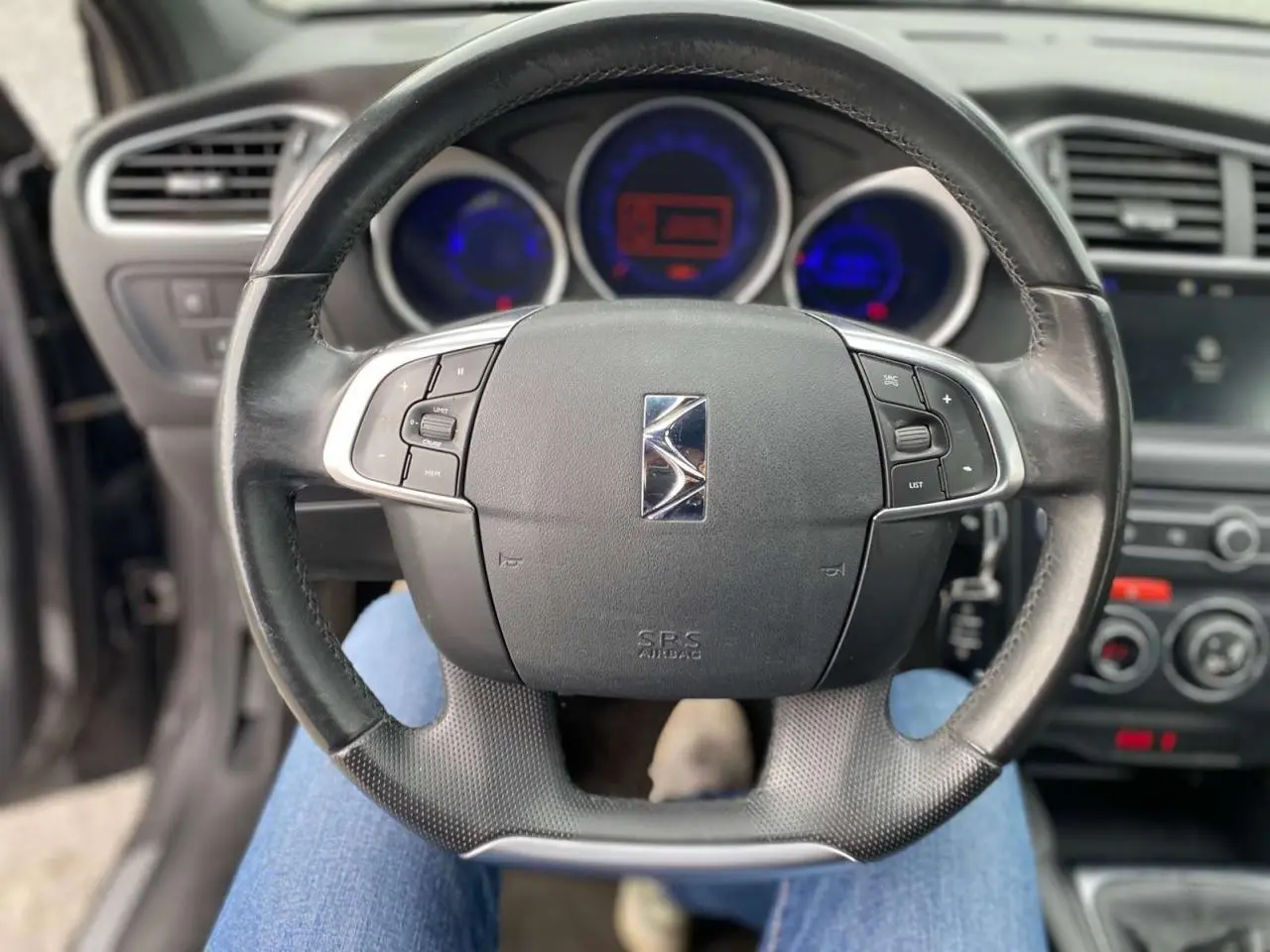 Vue rapprochée du volant noir du DS4 2016 avec commandes intégrées et tableau de bord lumineux en arrière-plan.